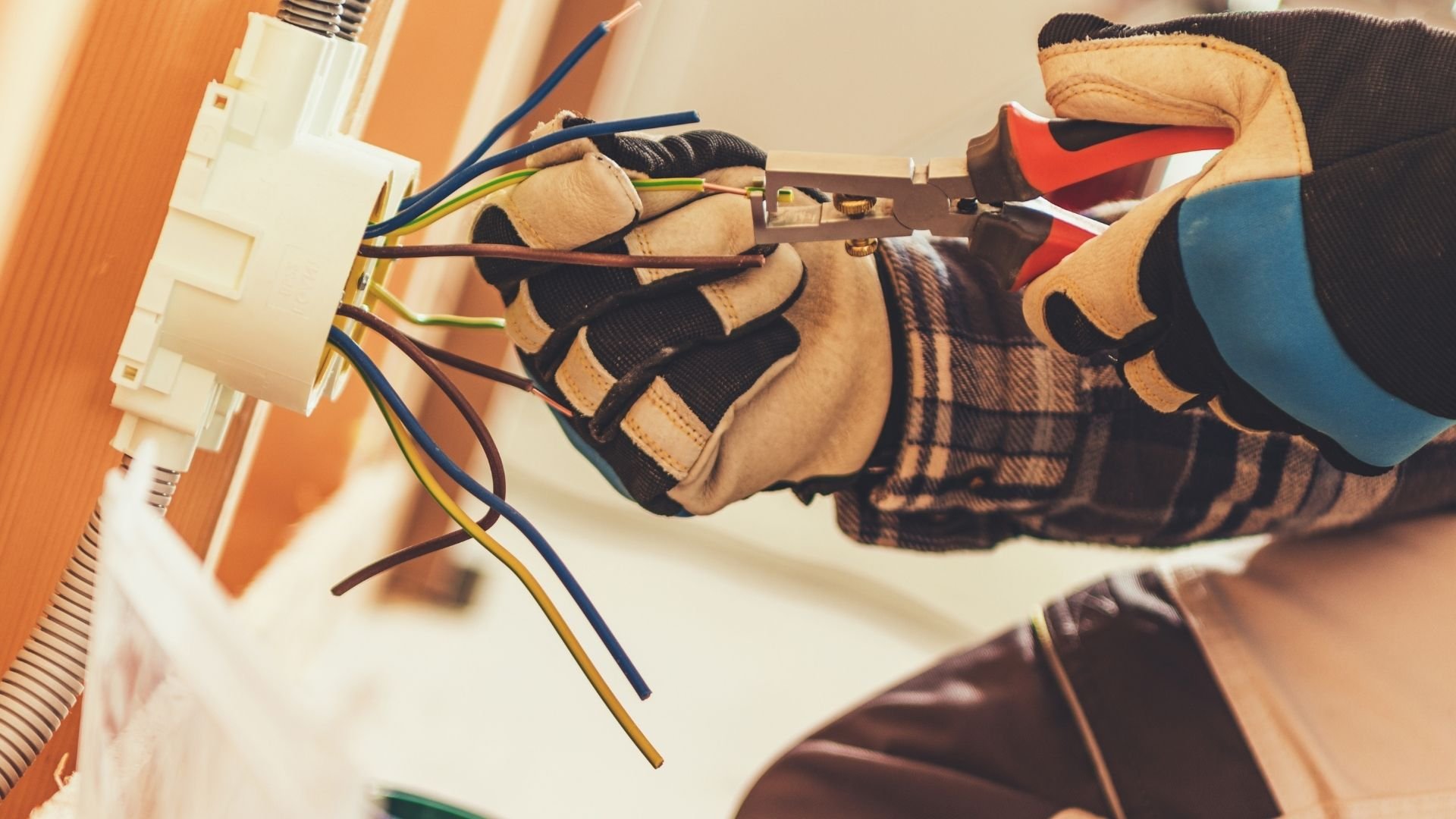 Electrician wearing protective gloves connecting wires to electrical outlet