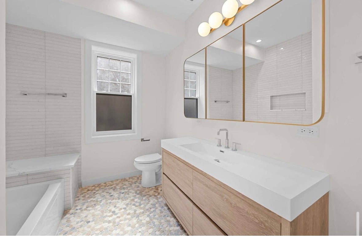 Modern bathroom with white tiles, wooden vanity, and gold-framed mirror
