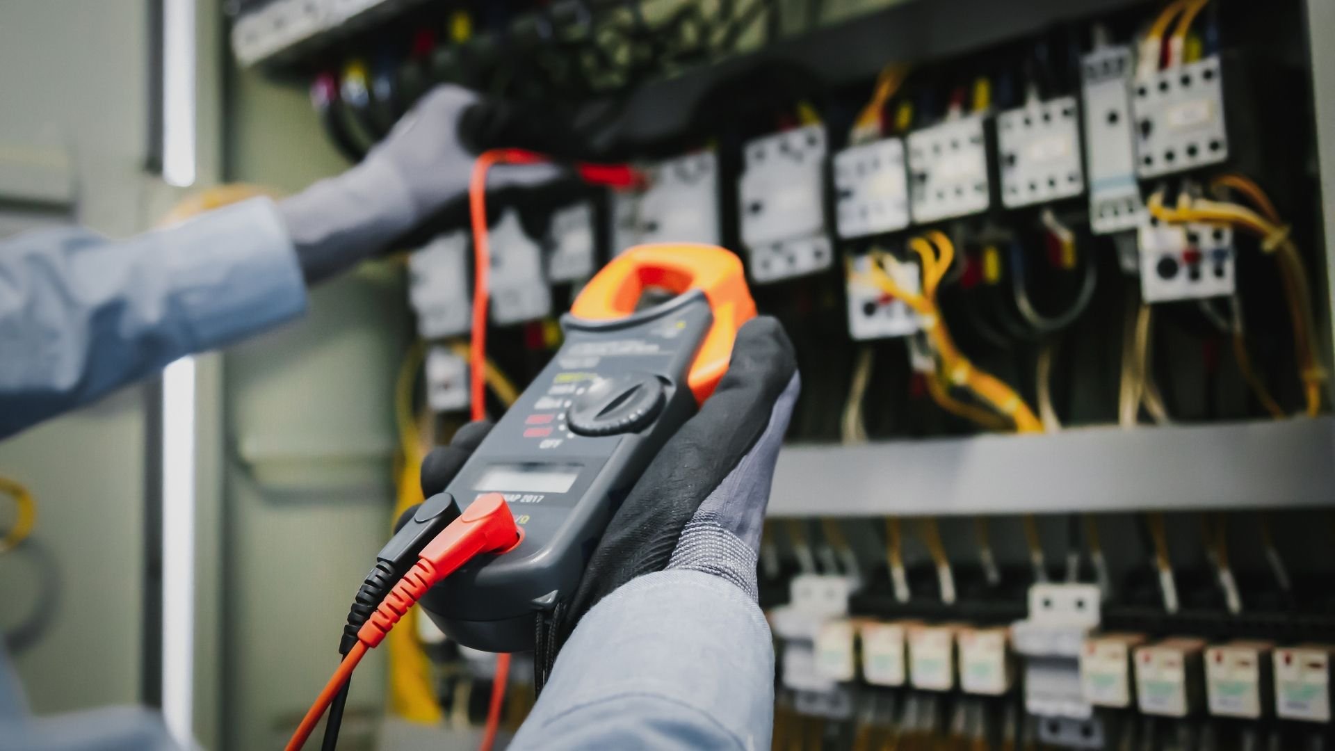 Electrician using multimeter to test electrical panel with safety gloves
