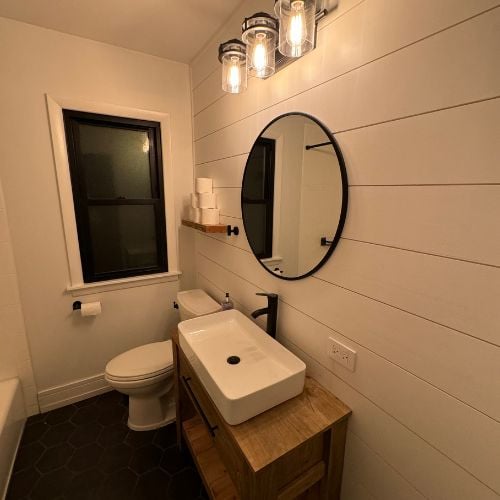 Modern bathroom with round mirror, wooden vanity, and industrial light fixtures