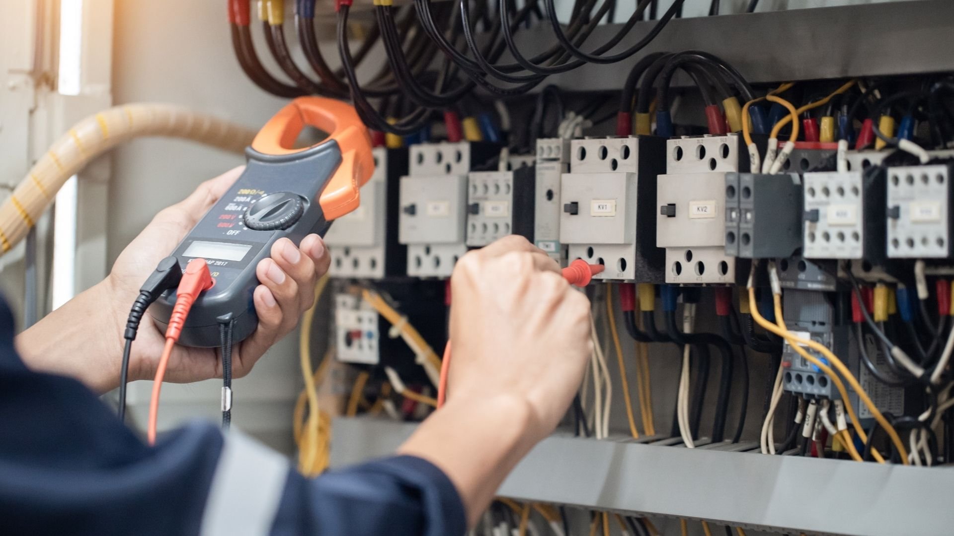 Electrician using clamp meter to test electrical panel with multiple contactors