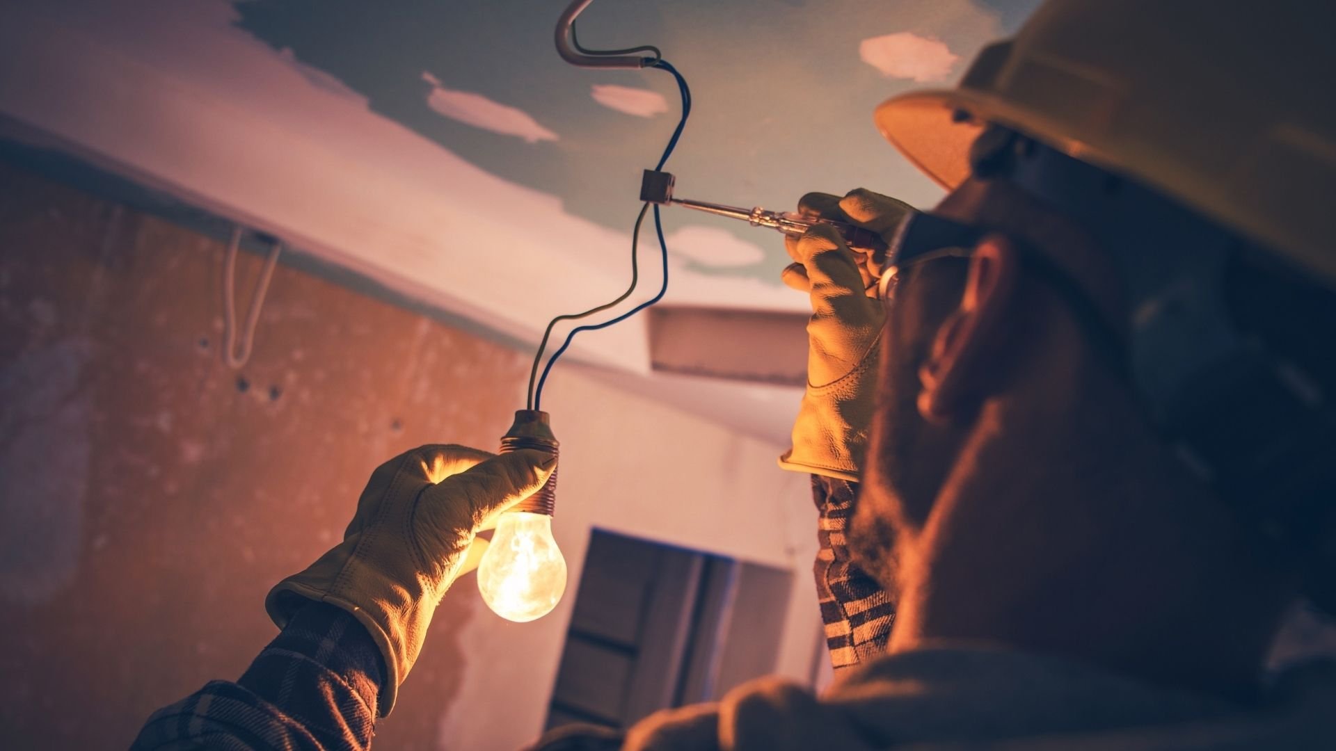 Worker installing light bulb with gloved hands in warm-toned workspace