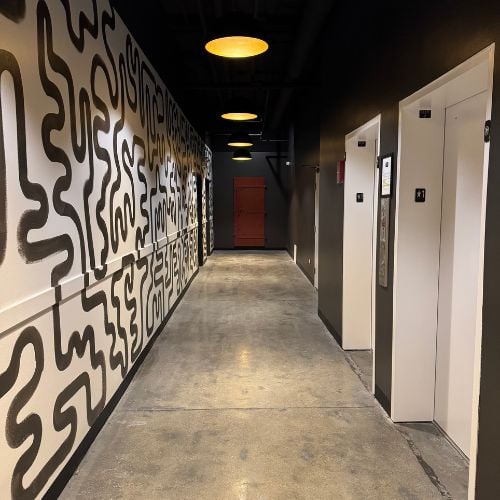 Modern hallway with abstract wall art, yellow lights, and white elevator doors
