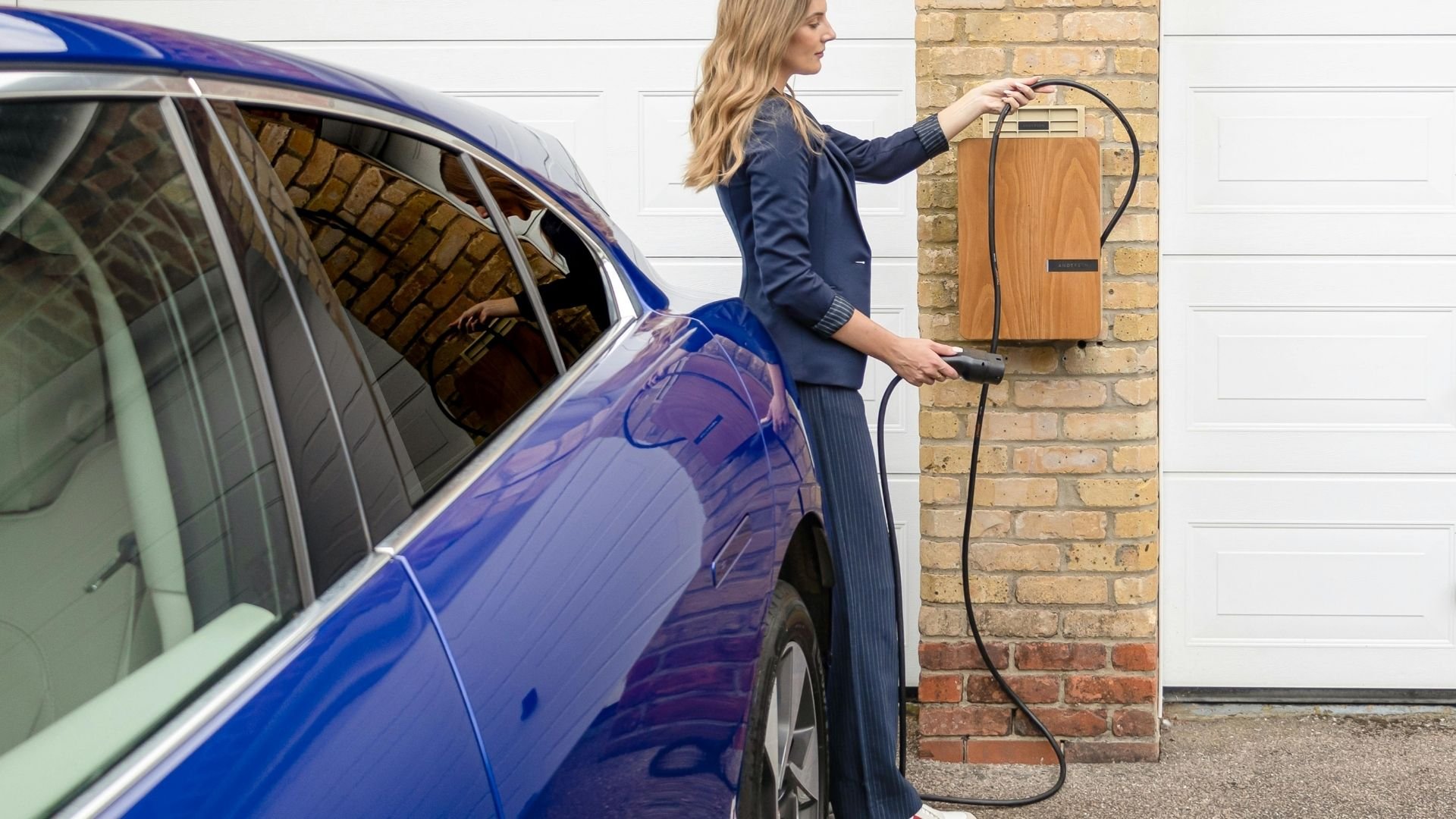 Woman charging blue electric vehicle at home charging station