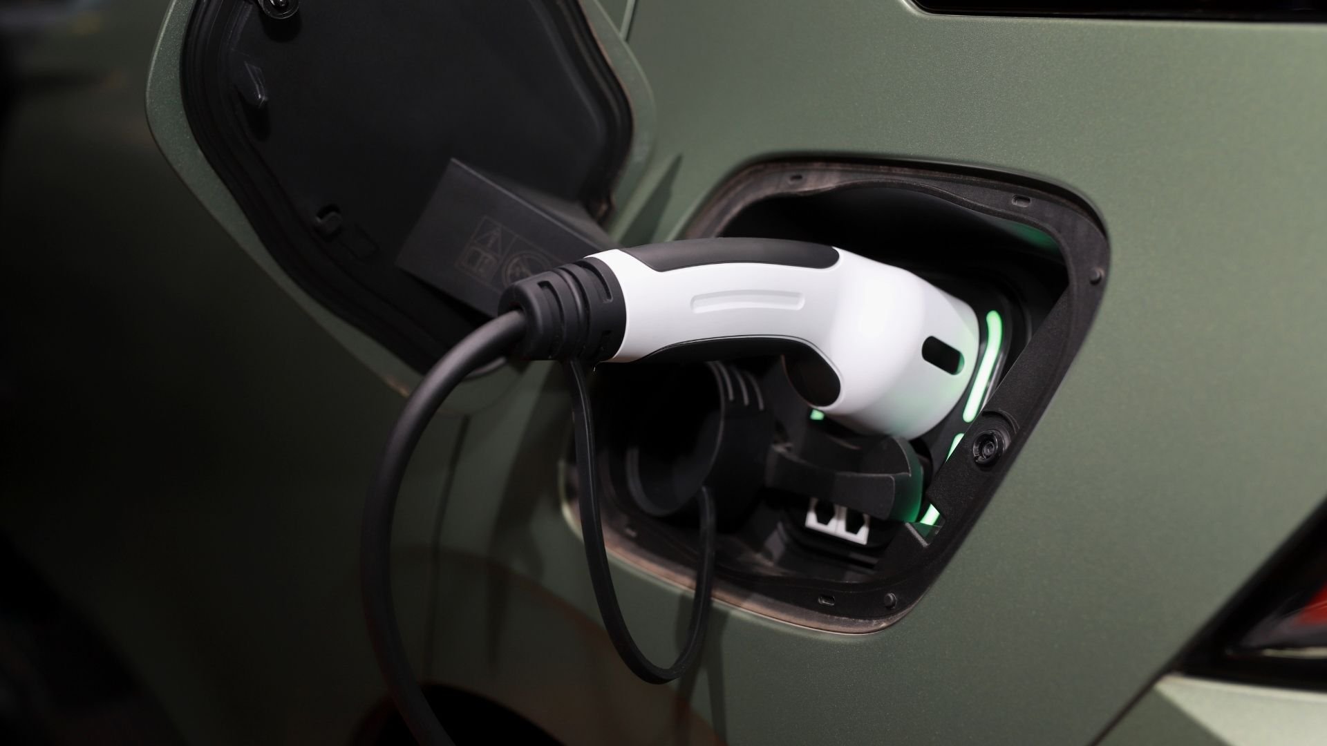 White electric vehicle charging cable plugged into green car's charging port
