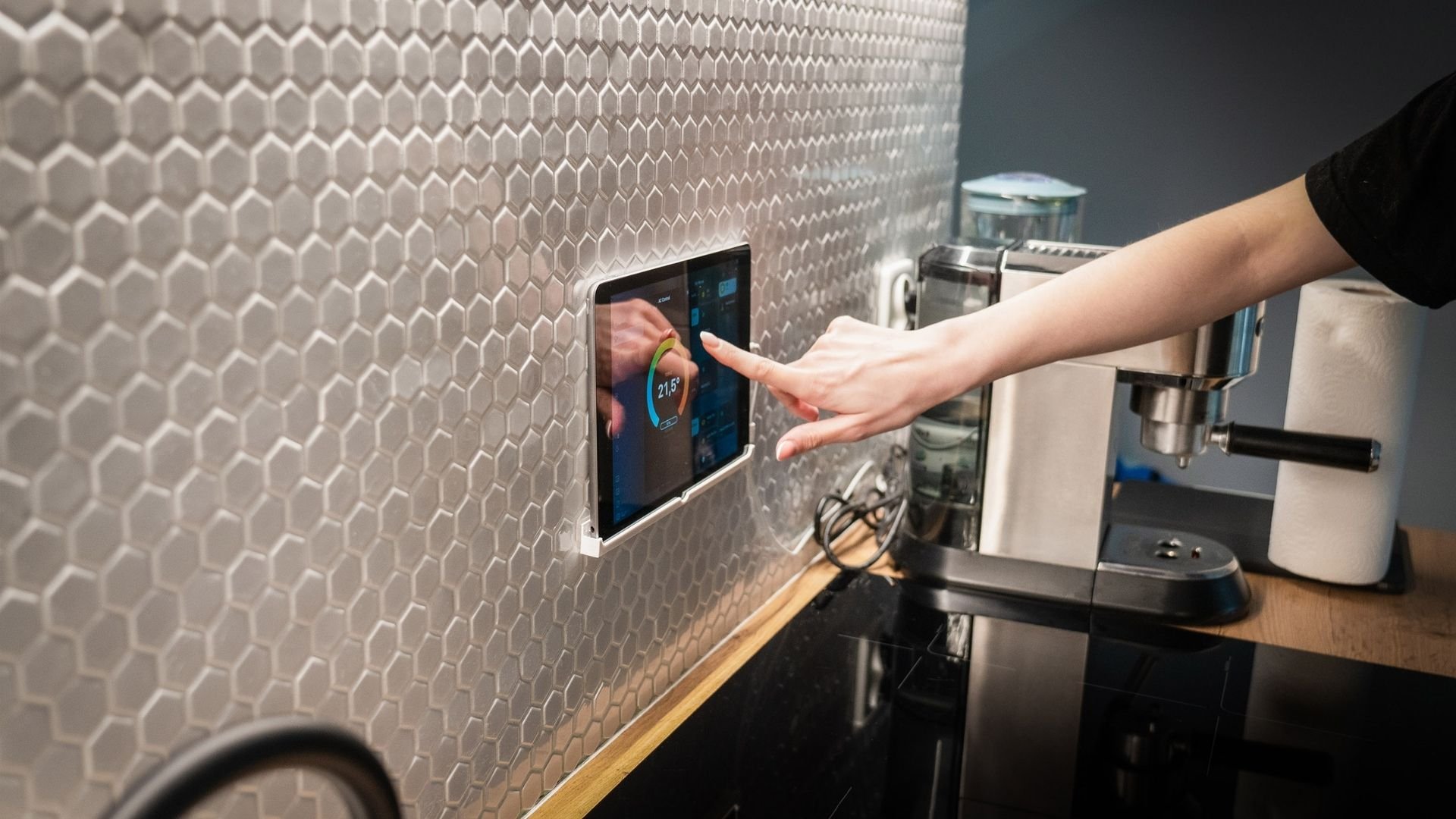 Hand adjusting digital thermostat on hexagonal tiled kitchen wall