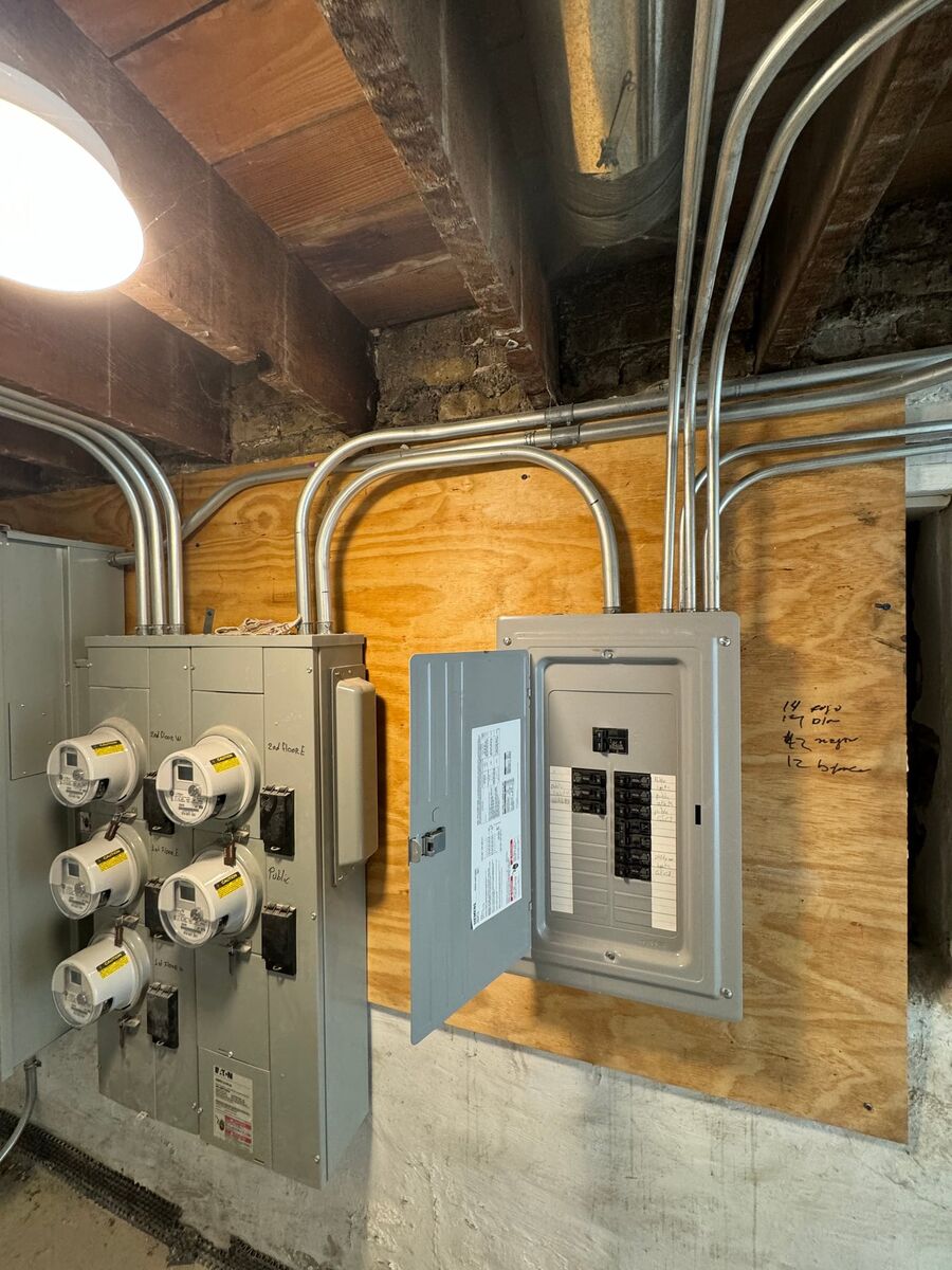 Old fuse boxes beside a new electrical panel during a safety inspection