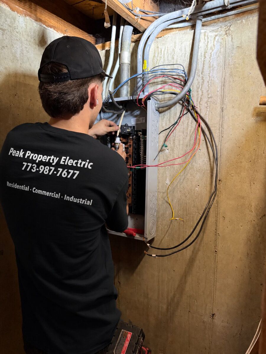 Peak Property Electric electrician in a branded shirt servicing an electrical panel